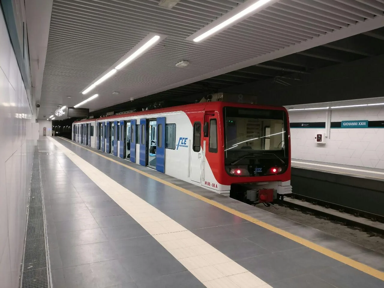 Un treno bianco, rosso e blu della metropolitana di Catania con le porte aperte, fermo alla banchina della stazione sotterranea Giovanni XXIII
