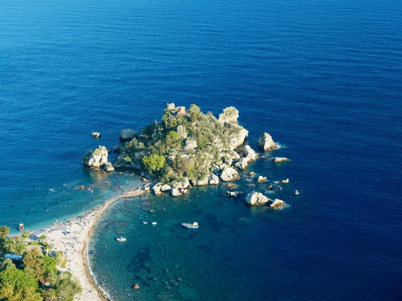 L'Isola Bella di Taormina vista dall'alto: l'isolotto verde e roccioso unito alla spiaggia da una sottile lingua di ciottoli, circondato da acqua turchese e blu intenso